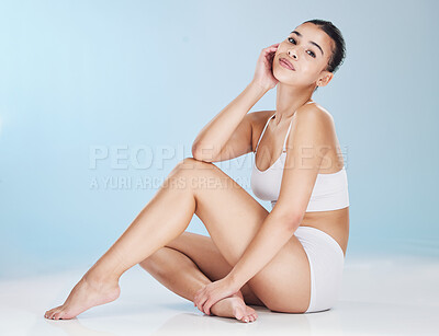 Buy stock photo Portrait of a beautiful young woman posing in underwear while sitting in studio isolated against a blue background. Beauty shot of a confident and flawless model with soft, smooth and silky skin