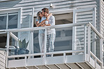 Love, kiss and couple on balcony with coffee, espresso or cappuccino in home. Tea, relax and romantic man and woman enjoying quality time together, bonding or affection with view on holiday in house.