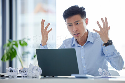 Frustrated, annoyed and irritated business man gesturing in anger while working on his laptop. Young male worker feeling upset or struggling with an internet crash while at his desk in the office