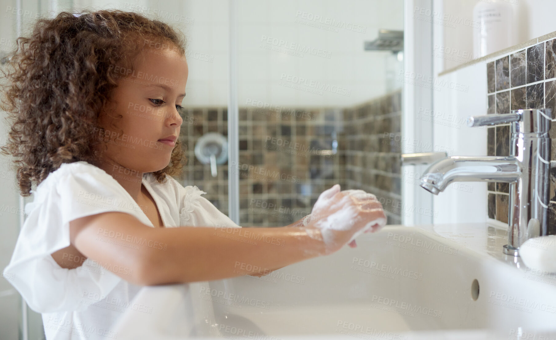 Buy stock photo Little girl washing hands with water and soap in bathroom at home. Learning about and practicing good hygiene  keeps us healthy. Child cleaning fingers at a basin or sink