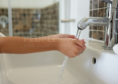 A closeup of a young girl washing her hand at the sink inside a bathroom with running tap water. A child practicing hygiene and cleanliness by rinsing her palms for virus prevention