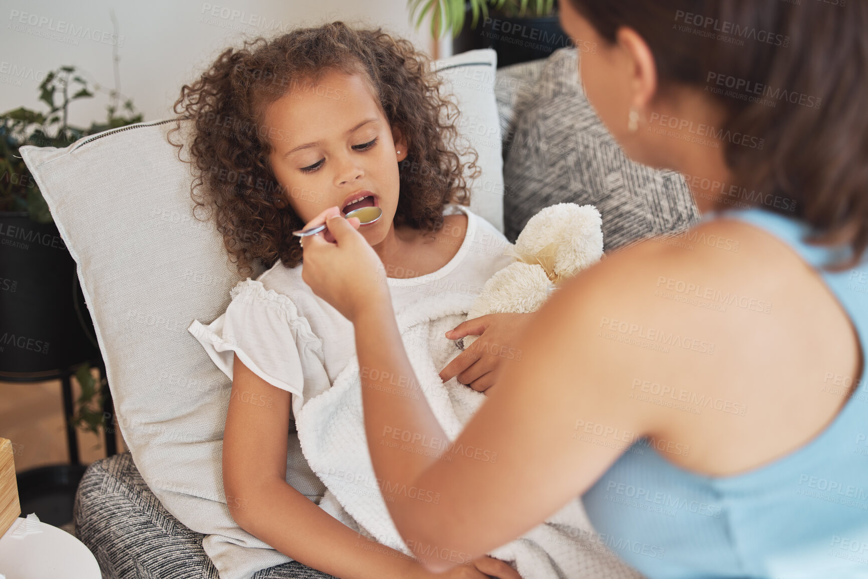 Buy stock photo Sick child drinking medicine, soup or food lying on the sofa for health and recovery inside their home. Ill girl being fed from a spoon by caring, loving and affectionate mother feeding her