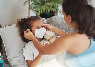 Buy stock photo Health care for sick, tired little girl with covid wearing face mask while resting on a sofa at home with worried mother. Anxious parent helping her unwell daughter to protect and stop virus spread