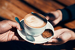 Closeup of hands holding and giving a cappuccino or flat white to a customer at a cafe. Hot beverage with creative plant image in milk foam. A morning coffee drink made by a barista in a restaurant.