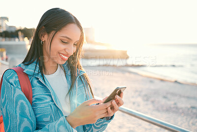 Happy woman outdoors holding phone and texting, searching or sharing location on an online social media app. Single female enjoying the beach view and sharing experience on her tourism blogging site