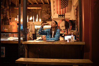 A young and happy woman eating pizza sitting alone in an empty and dimly lit American restaurant. A female relaxing and enjoying delicious food late at night in a dark and cosy pizzeria.