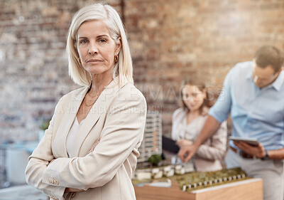 Buy stock photo Serious, confident and assertive senior project manager leading team in planning. Female urban planner standing as her employees design a model in the background. Top executive, architecture firm
