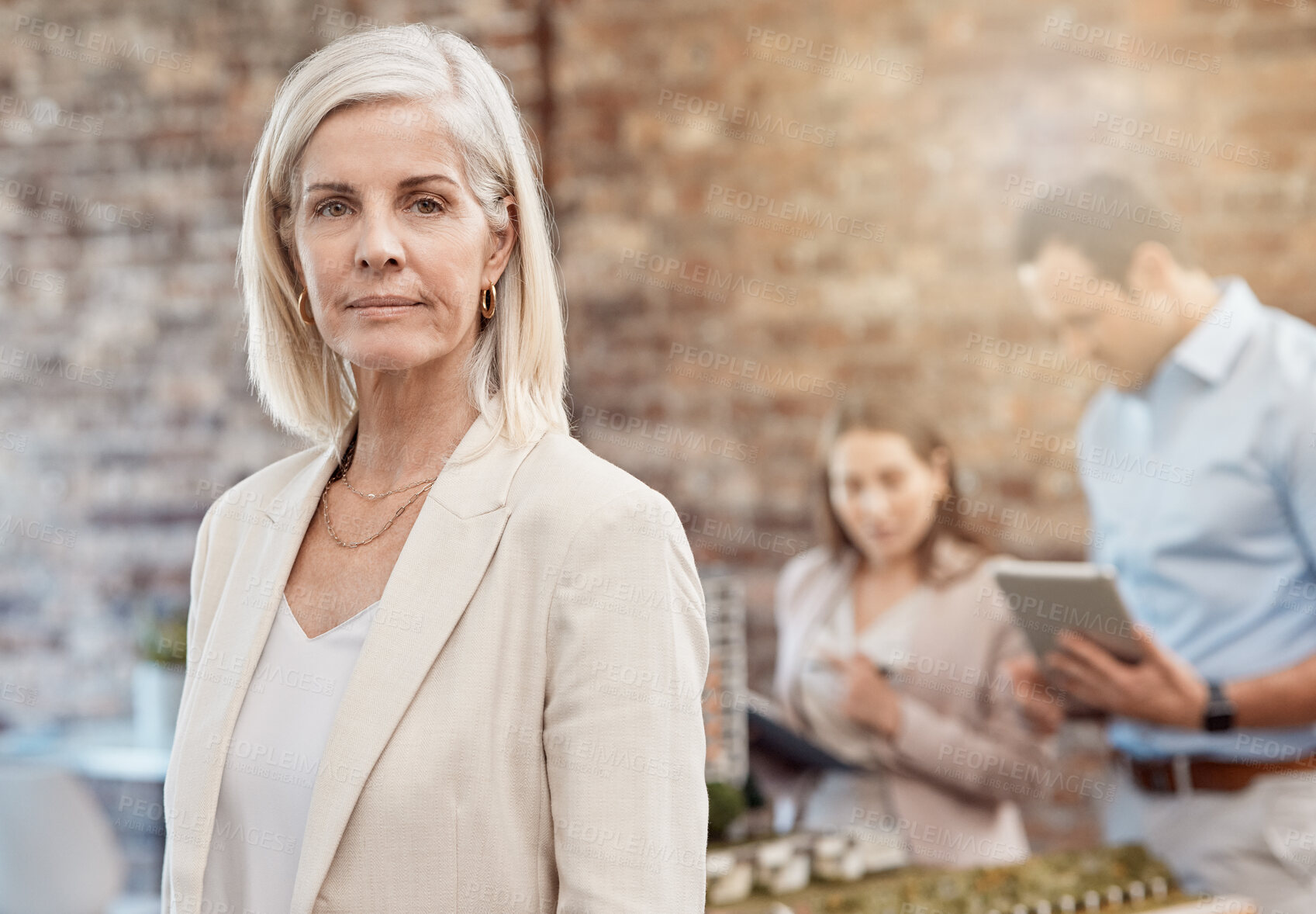 Buy stock photo Serious, confident and executive professional or manager leading her busy team in planning. Mature urban developer standing as her employees design a model in an architecture firm in the background