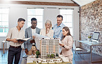 A diverse team of architects working on a building model together inside the office. A group of engineers planning a reconstruction or design  project of an apartment block with blueprint documents  