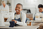 Happy, creative black fashion student or designer sitting and smiling in class by a sewing machine working on clothes. Isolated portrait of beautiful African American tailor in a factory or studio.
