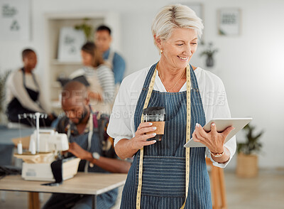 Buy stock photo Senior fashion designer reading online orders from a handheld tablet inside her shop. Old female clothing producer smiling about her success while holding coffee. A happy mature creative entrepreneur