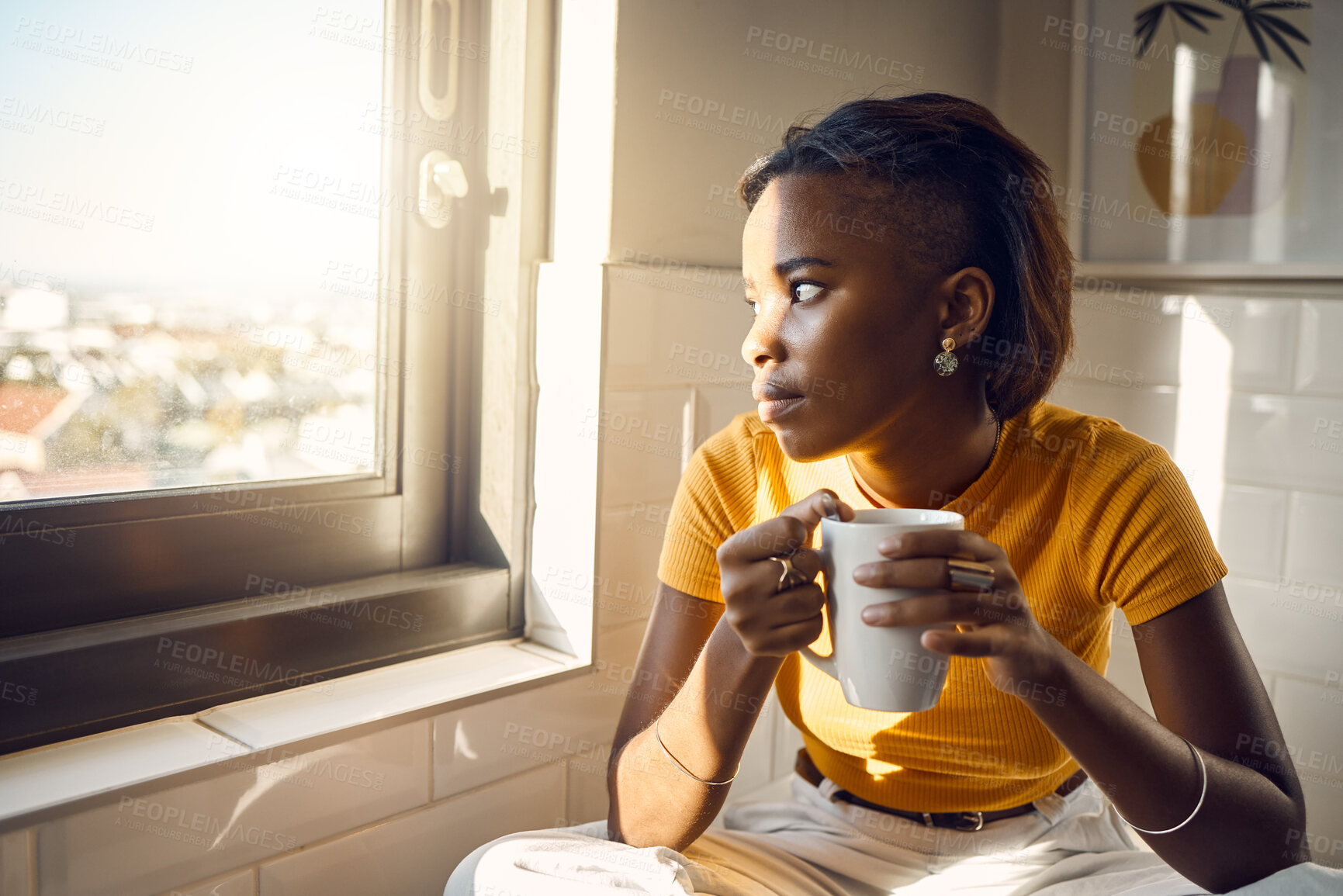 Buy stock photo A thinking and coffee drinking black woman enjoys her morning routine while gazing outside a window on a bright sunny day. Beautiful female looks thoughtfully towards city while sitting at home