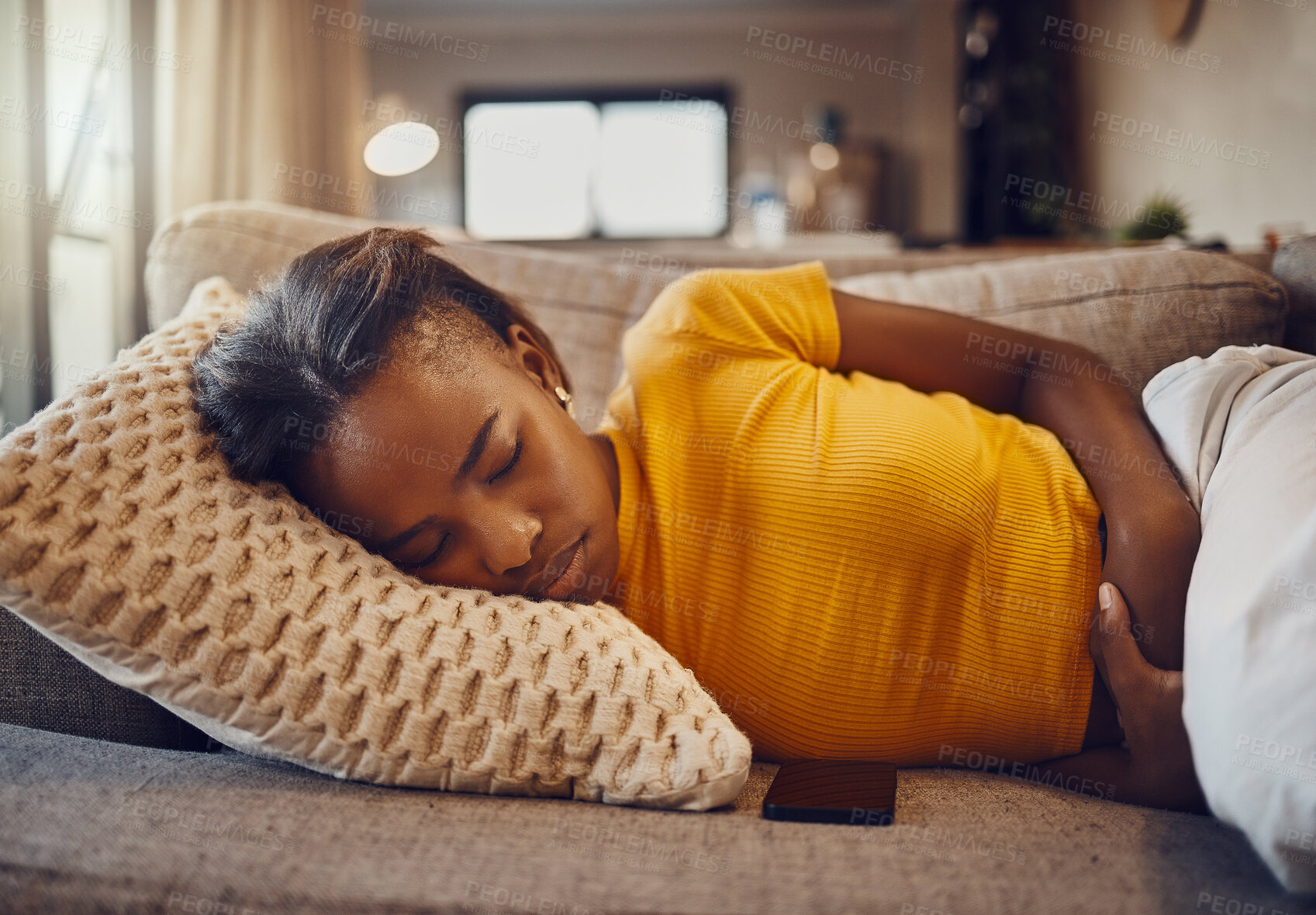 Buy stock photo Stomach pain, illness and sickness causing a tired, young and sleepy black woman to sleep, nap and rest on a couch at home. Relaxed, sick or ill female suffering from covid fatigue while napping