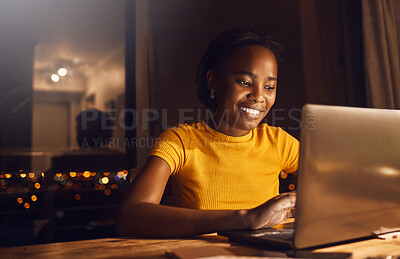 Young, happy and beautiful woman working and studying at night to make deadline for online course. Smiling and positive black girl on a laptop finishing her project while sitting at her desk at home