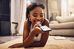 Girl texting, chatting and browsing social media on her phone while relaxing at home. Young woman searching an online app, enjoying free time and having fun with an app on her living room floor