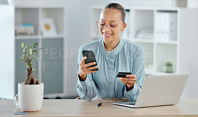 Female executive online shopping, buying with a corporate credit card on a phone. A smiling woman paying business bills, sitting at office desk with laptop. Happy lady making a purchase on a website.