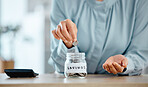 Savings, budget and economical woman putting coins in a jar at home. Closeup of woman calculating her expenses and saving money for future investment managing her house finances