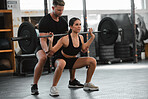 Healthy, fit and active woman exercising, weight training and squatting with her fitness and personal trainer at the gym. Athletic young female athlete lifting a barbell with her bodybuilder coach