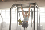 A fit, active and athletic female lifting herself in the gym exercising to improve strength and conditioning. Young woman athlete training with equipment doing pull ups as part of her workout routine