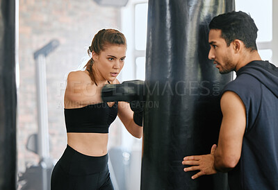 Buy stock photo Fit female learning boxing on a punching bag and getting fitness training advice from her personal trainer at a gym studio. Strong boxer with slim body practicing for a fight with her fighting coach