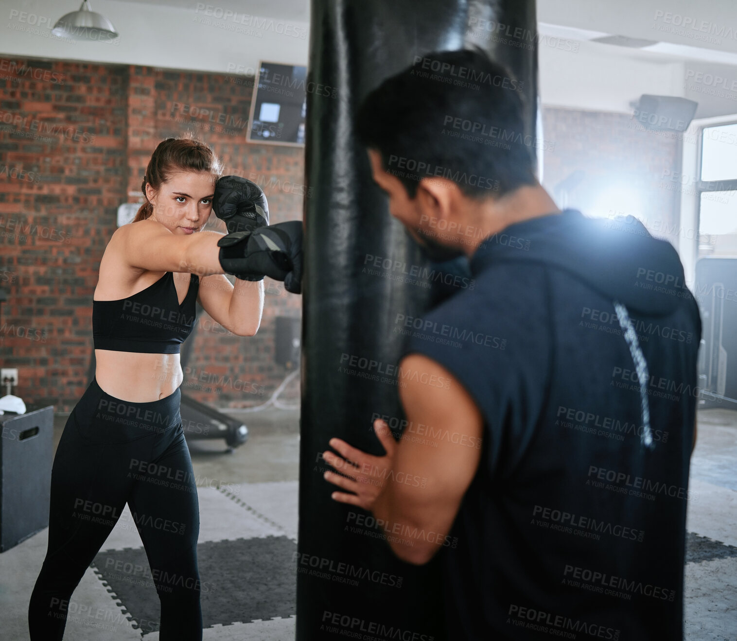 Buy stock photo Fit female boxer boxing a punching bag with fitness training advice from her personal trainer at a gym studio. Strong, serious and confident athlete with a slim body gets help from her coach