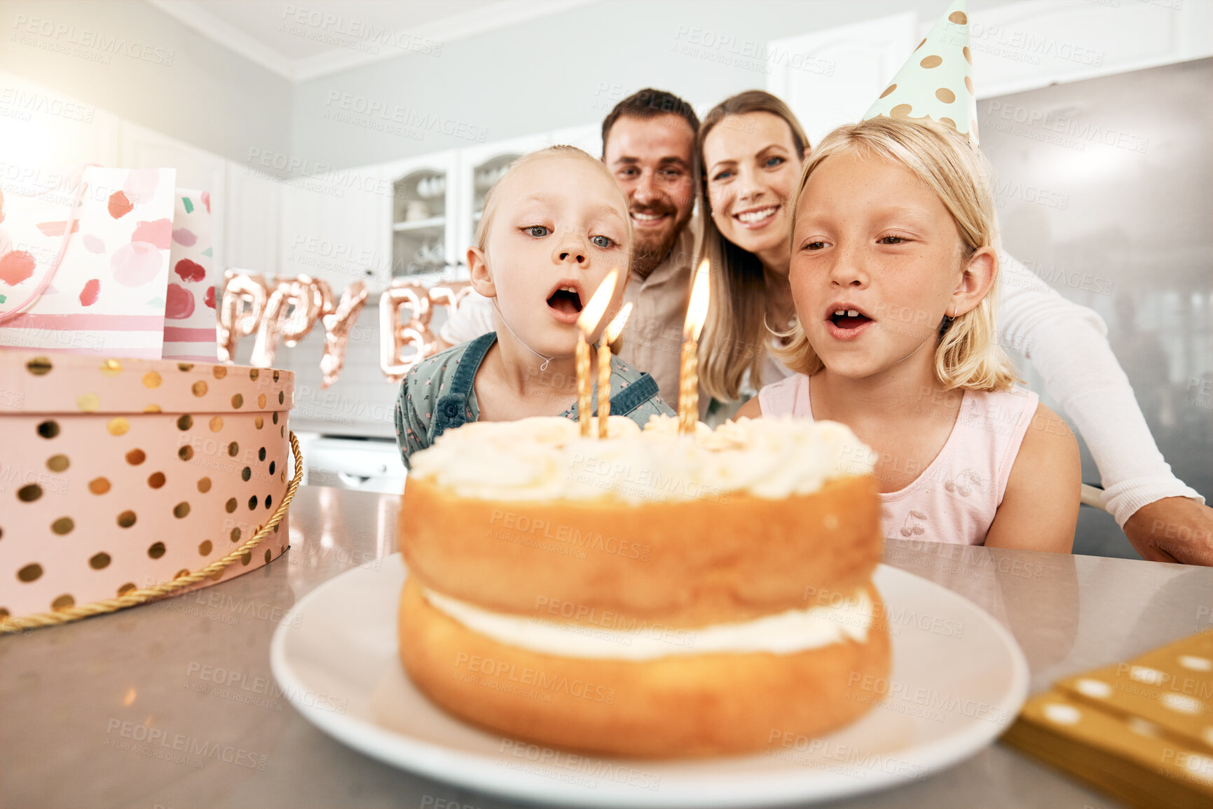 Buy stock photo Birthday, cake and celebration with a girl and her sister blowing out candles and making a wish with her family in the background. Celebrating, party and growing up with children and their parents