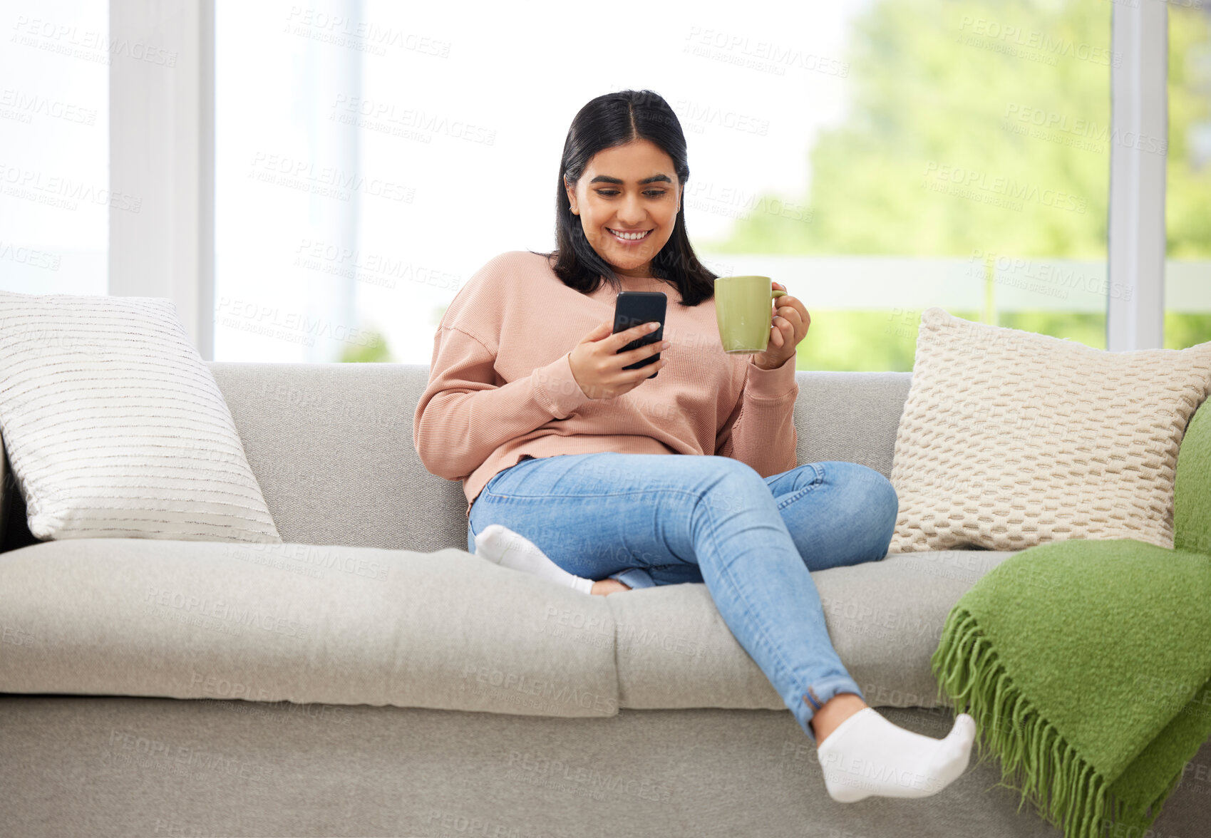 Buy stock photo Rest, relaxation and carefree with a young woman typing on a phone, drinking coffee and comfortable on the sofa at home. Relaxed female browsing social media or typing a message with a cup of tea