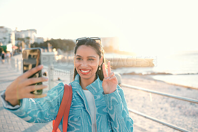 Buy stock photo Smiling, trendy and fun woman, tourist or influencer taking selfie with peace sign gesture on phone for social media, video call or photo. Exploring, traveling and sightseeing at promenade outdoors