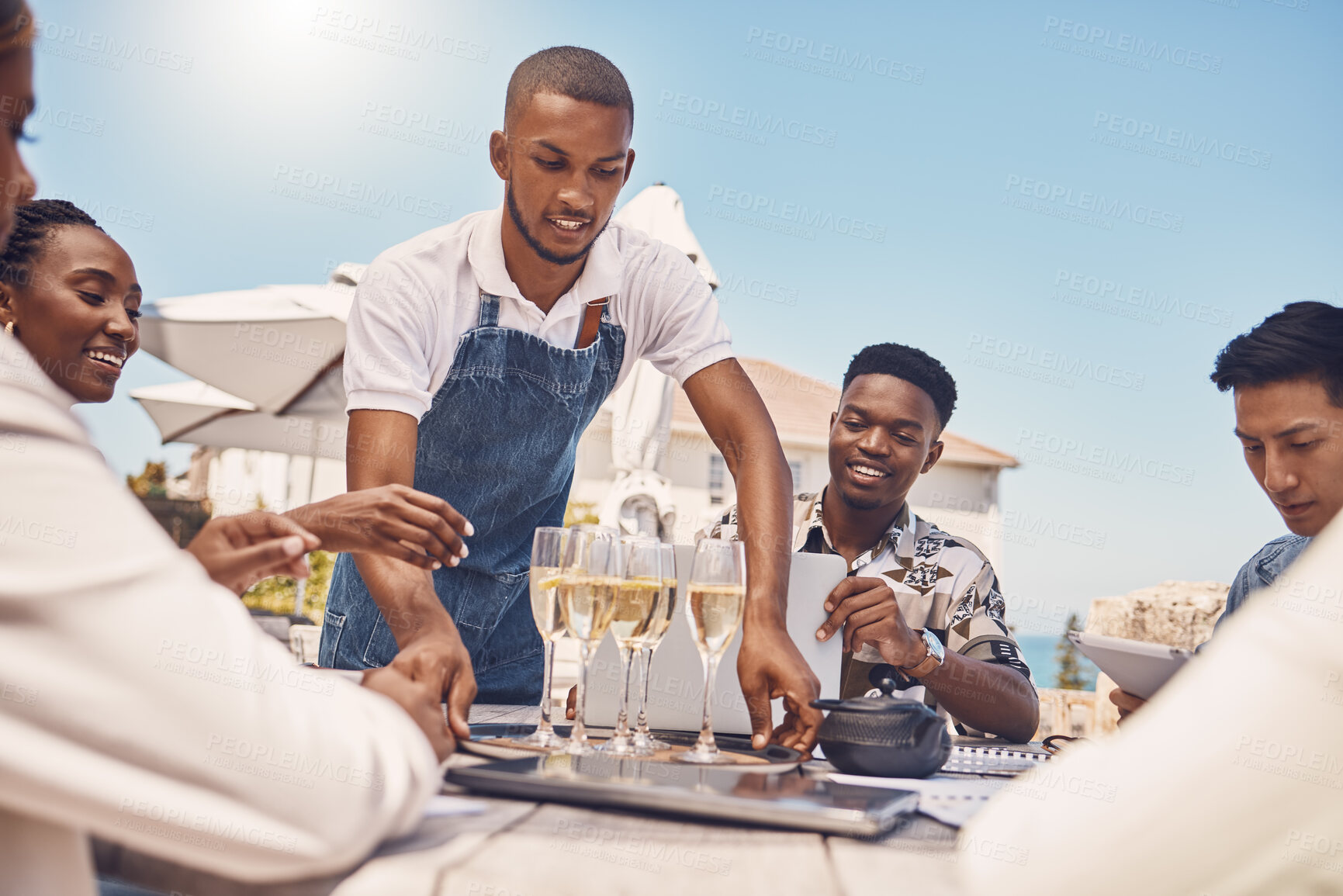 Buy stock photo Beach restaurant, waiter and champagne celebration with friends. Hospitality, fine dining and a relaxing outdoor meal with people. Summer holiday or lunch break outside with view of the ocean.