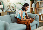 Browsing for movies to watch online on a tablet, streaming videos and scrolling on social media while relaxing on the couch alone at home. Stylish, trendy and casual female browsing the internet