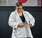 Female professional karate student dressing, wearing and preparing for practice, fight or training match in dojo. Woman mix martial art athlete tying uniform before competition or exercise workout