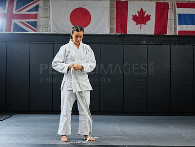 Buy stock photo Professional karate student dressing and prepare for practice in a dojo or club. Female mix martial art athlete tying belt in training for a fight, competition or exercise workout in a sport studio