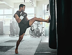 Male athlete kicking a punching bag in a gym while practicing, training and fitness exercise. Strong professional fighter or athletic man in a health and wellness club busy with a combat workout