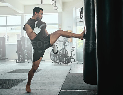 Buy stock photo Male athlete kicking a punching bag in a gym while practicing, training and fitness exercise. Strong professional fighter or athletic man in a health and wellness club busy with a combat workout