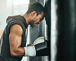 Strong, sweaty and fit male boxer resting while doing a cardio workout with a punching bag at gym. Sporty, active and determined athlete looking tired while exercising at a sports center for fitness.