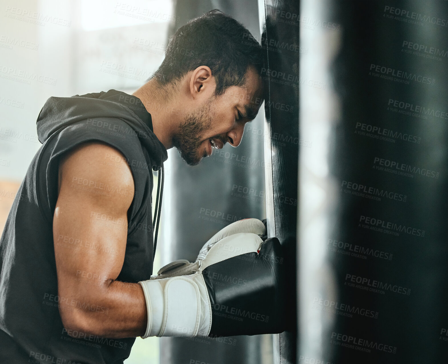 Buy stock photo Strong, sweaty and fit male boxer resting while doing a cardio workout with a punching bag at gym. Sporty, active and determined athlete looking tired while exercising at a sports center for fitness.