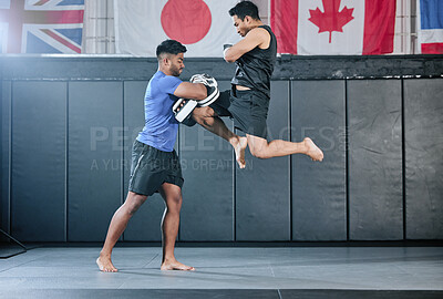 Buy stock photo Healthy professional coach sparring and training male kickboxer indoors. Practice sports, exercise and fitness. Two muscular men fighting, jumping and blocking kicks with discipline in class.