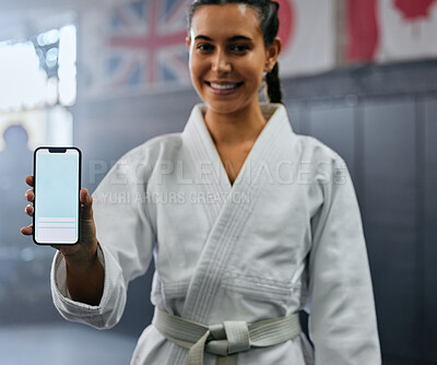 Buy stock photo Portrait of a female karate student holding tech with social media, looking active and fit at class. Blank screen on phone, showing a fitness app and training website while standing at a sports gym.