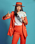 Happy, carefree and smiling woman holding and showing money, going on shopping spree and winning money prize while standing against a blue studio background. Portrait of a stylish female with cash
