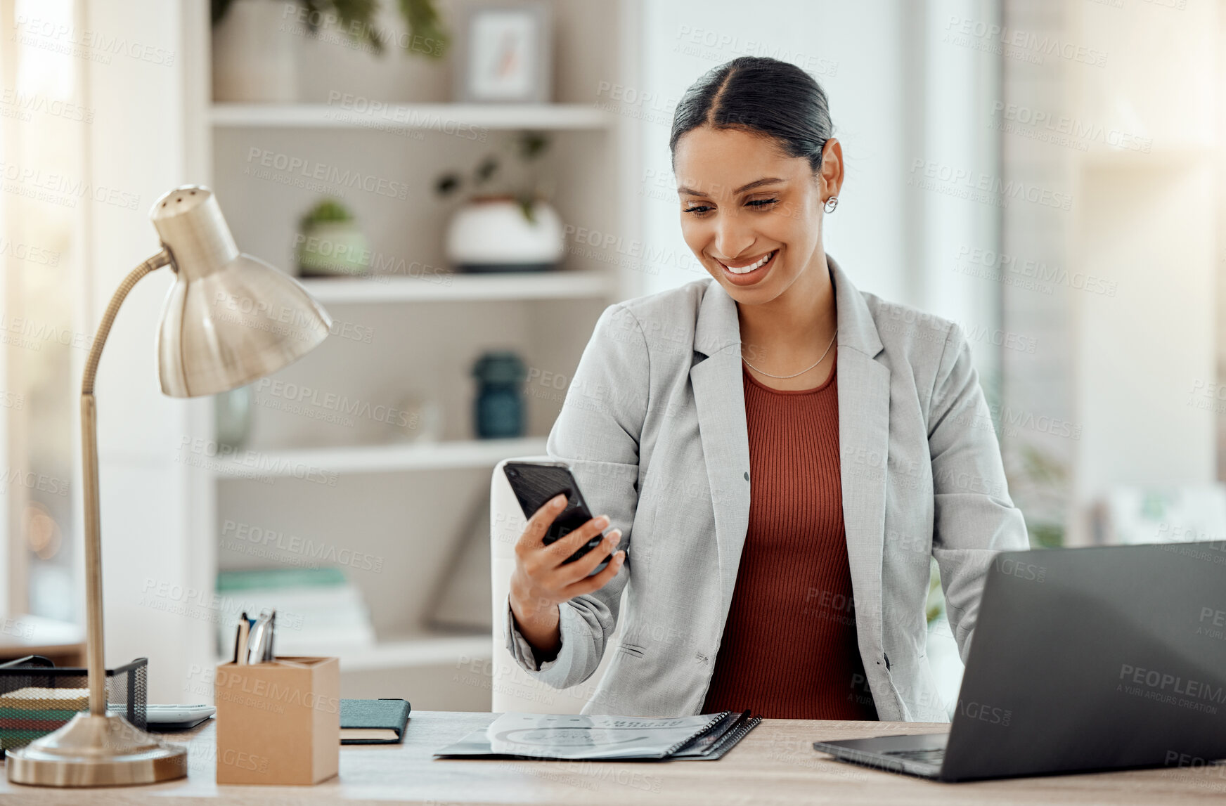 Buy stock photo Freelance and remote working business woman checking her phone, reading a message or sending a text in her home office. Motivated, happy and positive female professional sitting at her desk at work
