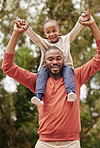 A young black father playing with his daughter happy, smiling and bonding while enjoying quality time together. A little girl, child or kid having fun and sitting on her dad or parent's shoulders