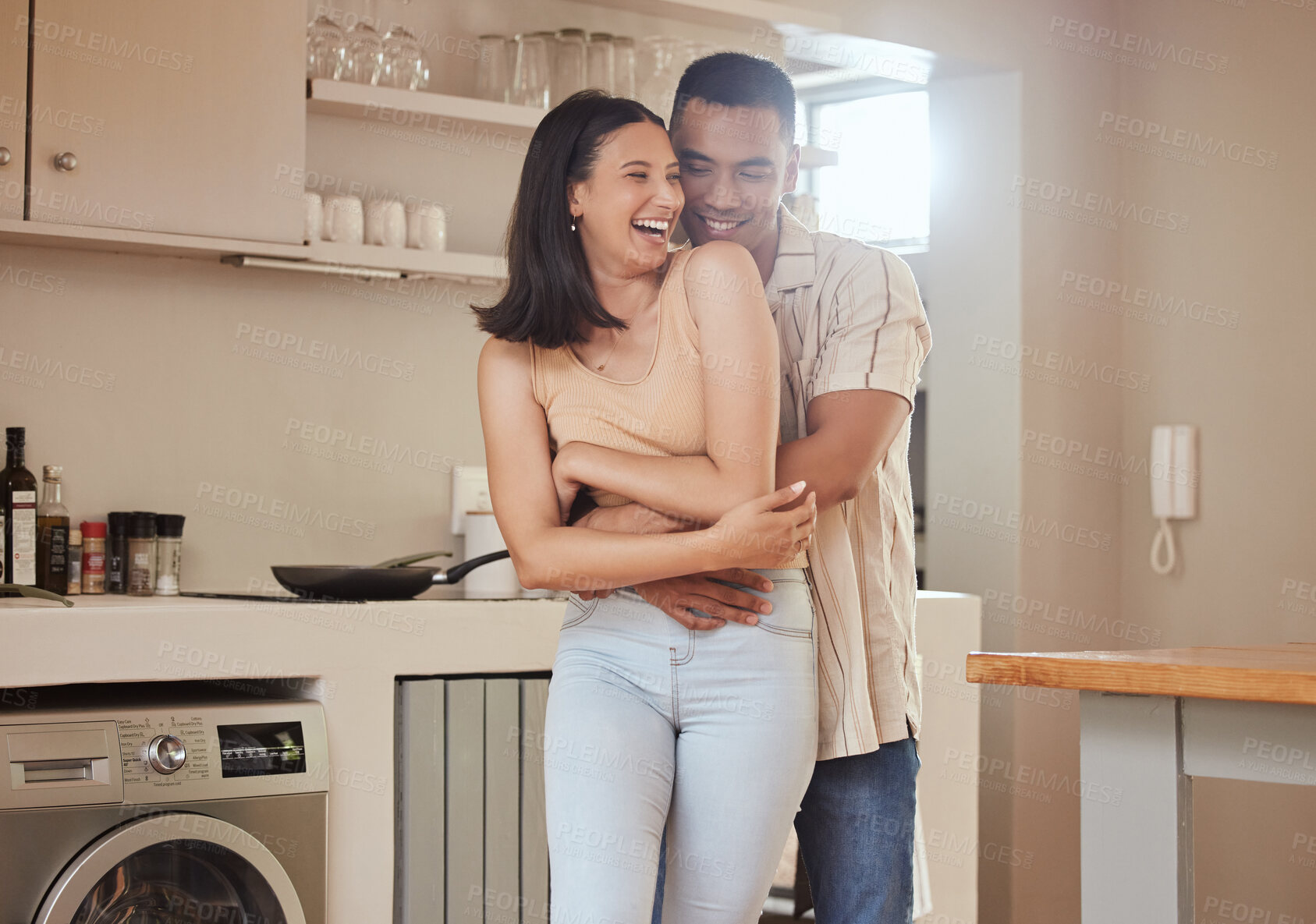 Buy stock photo Happy, romantic and in love couple smiling, hugging and embracing while relaxing together indoors at home. Young, loving and sweet husband hugging his carefree, laughing and fun wife in the kitchen 
