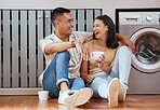Happy, carefree and romantic couple bonding, laughing and having fun while sitting on the floor. Loving cheerful husband and wife having a cup of coffee, talking and relaxing in the kitchen at home