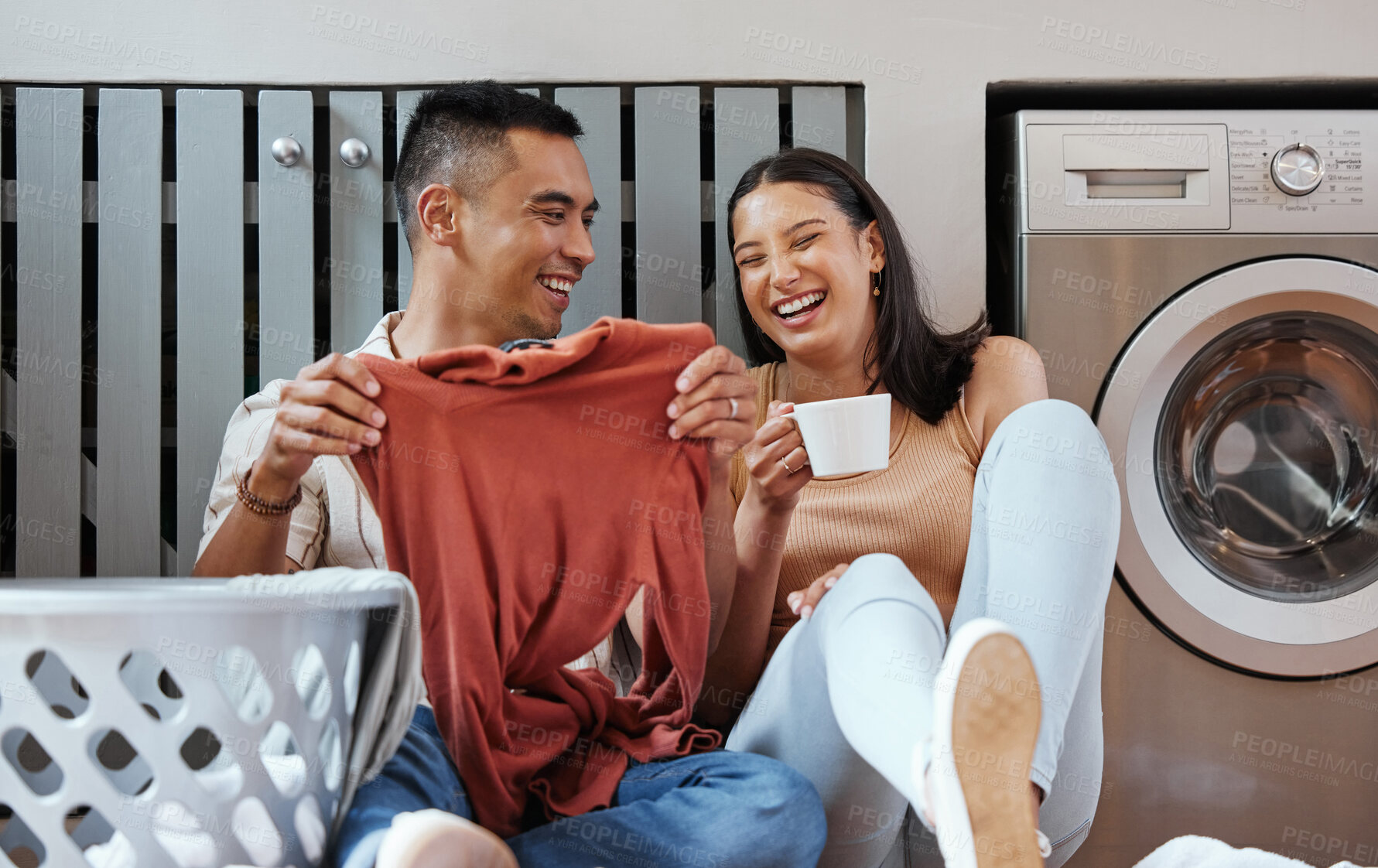 Buy stock photo Carefree and funny couple doing laundry and relaxing together at home in the morning. Silly, goofy and playful lovers laughing and giggling while cleaning the washing, and doing house chores