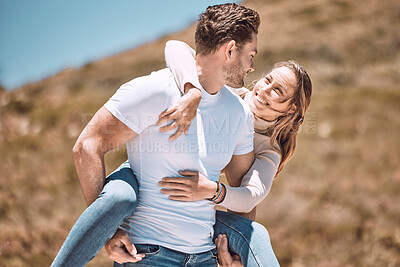 A young loving, affectionate and fun couple bonding while enjoying the day laughing outdoors in nature. Happy, in love and smiling man piggyback his wife while holding her outside on a valley or hill