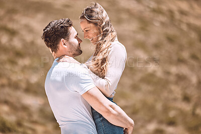 Buy stock photo A young loving, affectionate and caring couple bonding while enjoying the day outdoors in nature. Happy, in love and smiling man embracing his wife while holding her outside on a valley or hill
