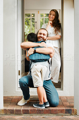 Dad hugging son about to leave for school or mother and father saying goodbye to child on front porch at home. Happy family greeting little boy with mother standing in doorway or house entrance.