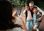 Mother taking a family photo on her phone of her happy little children and their father smiling together. Boy, girl and kids with their daddy smile for a picture taken by mom outside in the morning
