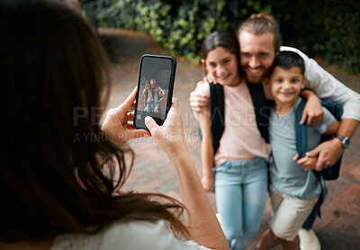 Buy stock photo Mother taking a family photo on her phone of her happy little children and their father smiling before school. Boy and girl siblings with their dad smile for a picture. Mom taking photos of kids