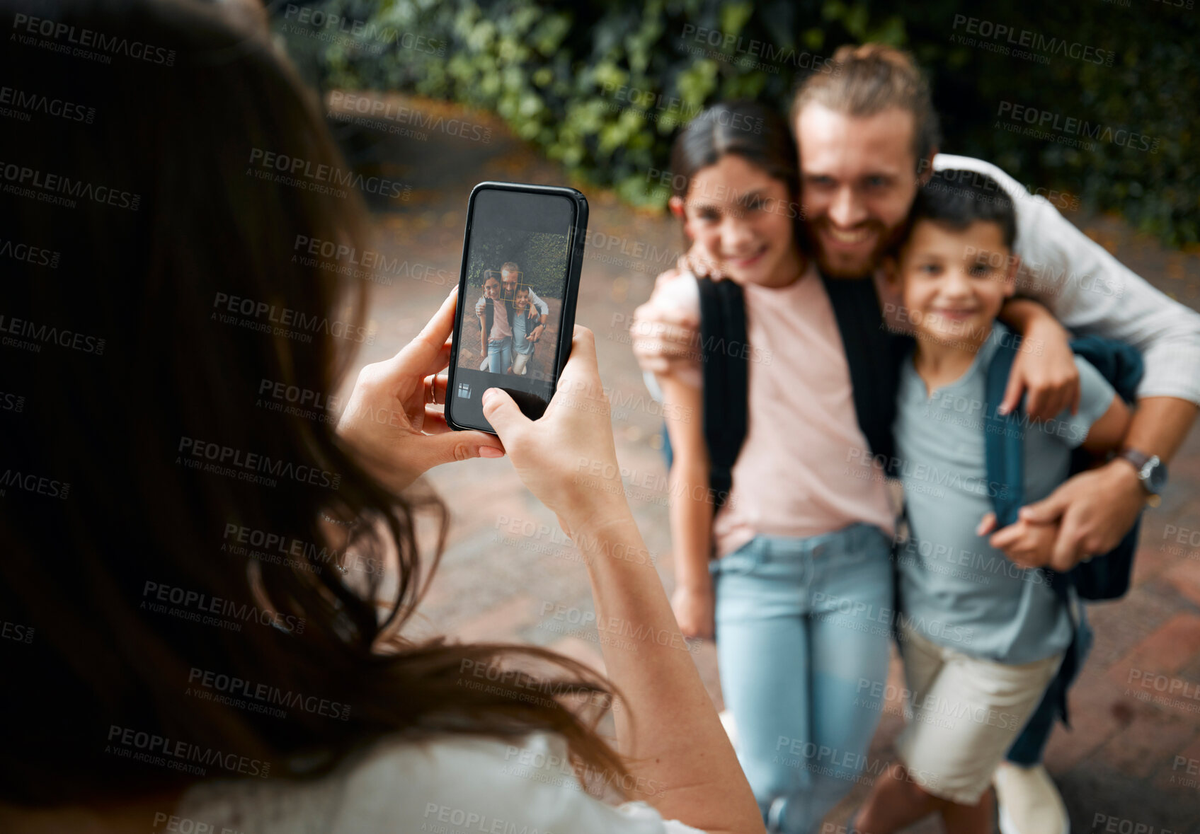 Buy stock photo Mother taking a family photo on her phone of her happy little children and their father smiling before school. Boy and girl siblings with their dad smile for a picture. Mom taking photos of kids